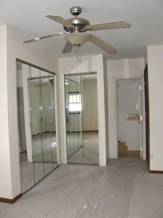 unfurnished bedroom with ceiling fan, light colored carpet, and two closets