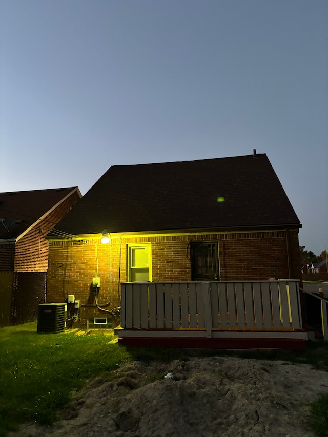 back house at dusk featuring a lawn, cooling unit, and a deck