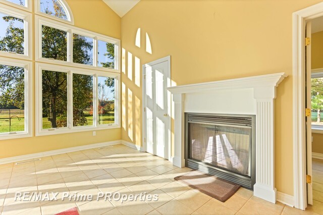 10300 Lange Rd, Birch Run, MI 48415 - unfurnished living room featuring healthy amount of natural light, baseboards, tile patterned flooring, high vaulted ceiling, and a glass covered fireplace