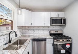 kitchen with light stone counters, white cabinetry, sink, and appliances with stainless steel finishes