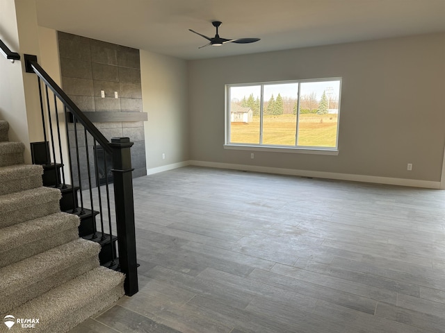 unfurnished living room with stairs, ceiling fan, baseboards, and wood finished floors