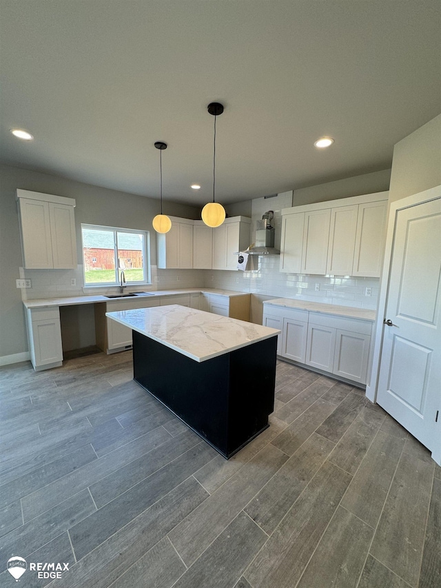 kitchen with a sink, tasteful backsplash, wood finish floors, and wall chimney range hood