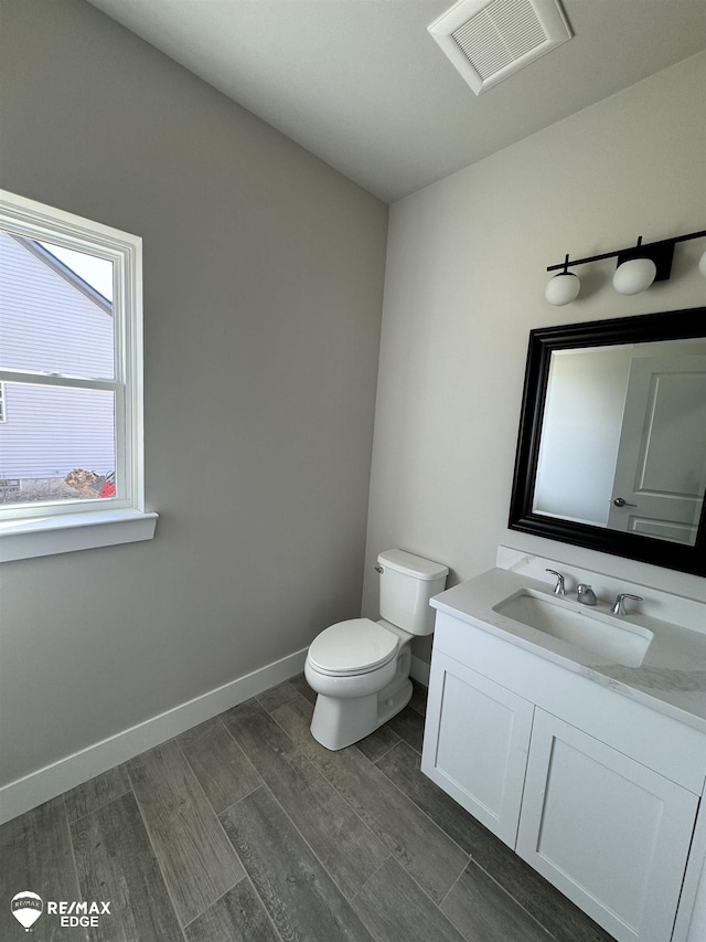 half bathroom with baseboards, visible vents, toilet, wood finished floors, and vanity