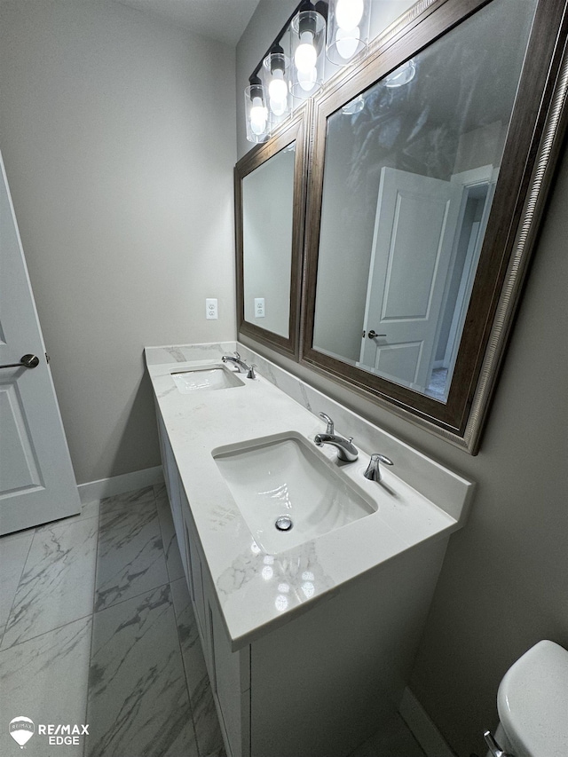 bathroom featuring double vanity, marble finish floor, baseboards, and a sink