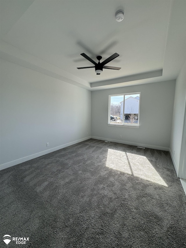 empty room with carpet, a raised ceiling, a ceiling fan, and baseboards