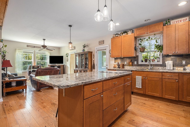 kitchen with pendant lighting, light hardwood / wood-style flooring, ceiling fan, a kitchen island, and a breakfast bar area