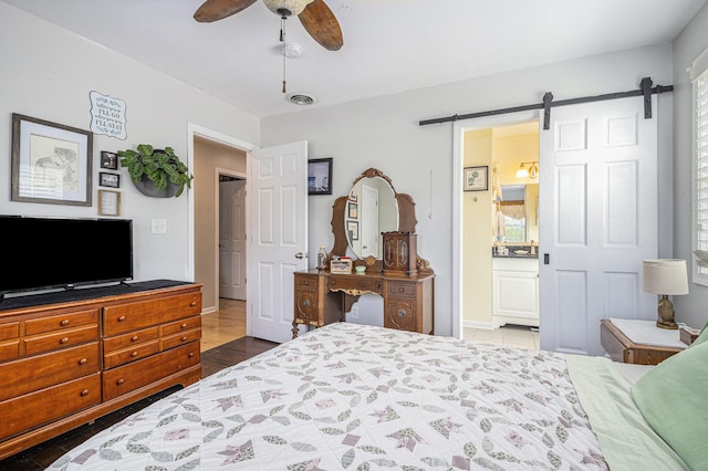 bedroom with ceiling fan, a barn door, dark hardwood / wood-style flooring, ensuite bathroom, and multiple windows