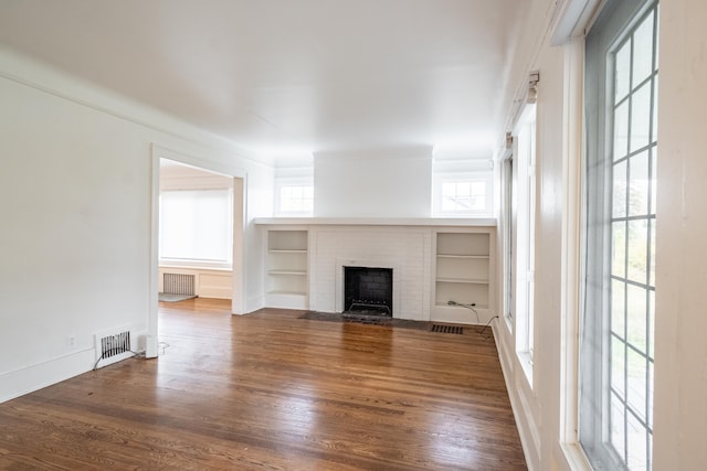 unfurnished living room with built in features, dark hardwood / wood-style floors, and a brick fireplace