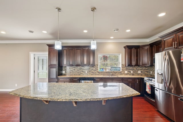 kitchen with dark wood finished floors, appliances with stainless steel finishes, a breakfast bar area, and light stone countertops