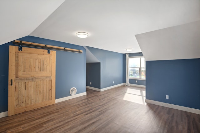 additional living space with baseboards, lofted ceiling, a barn door, and wood finished floors