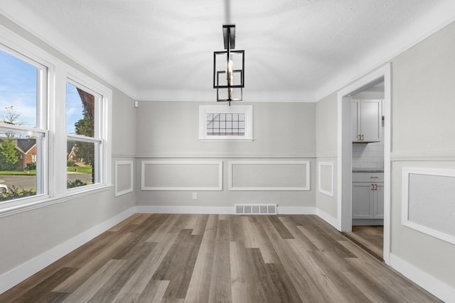 unfurnished dining area with wood-type flooring, a textured ceiling, and an inviting chandelier