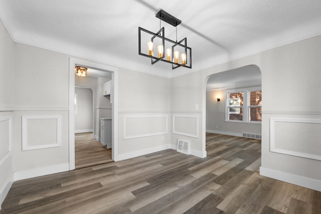 unfurnished dining area with a textured ceiling, dark hardwood / wood-style floors, and a notable chandelier