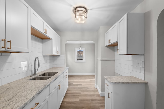 kitchen featuring decorative backsplash, sink, white cabinets, light hardwood / wood-style floors, and hanging light fixtures