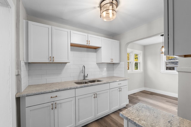 kitchen featuring white cabinetry, sink, hanging light fixtures, backsplash, and hardwood / wood-style flooring