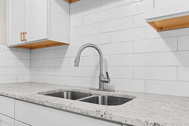 kitchen with backsplash, white cabinetry, sink, and light stone countertops