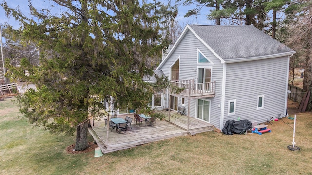 back of house with a balcony, a wooden deck, and a lawn