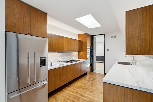 kitchen featuring a skylight, sink, stainless steel appliances, and light hardwood / wood-style floors