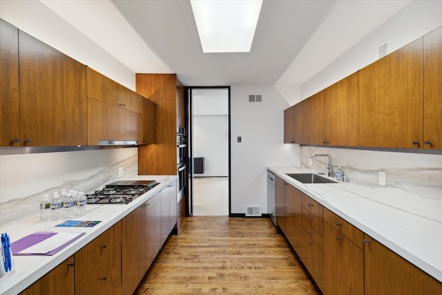 kitchen with light wood-type flooring, sink, range hood, and stainless steel appliances