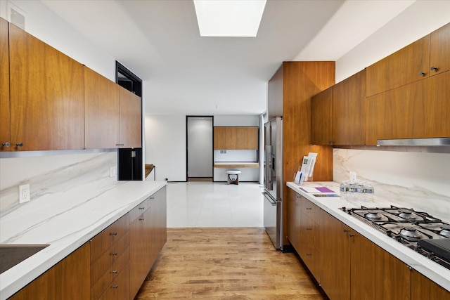 kitchen featuring stainless steel refrigerator with ice dispenser, a skylight, gas stovetop, sink, and light hardwood / wood-style floors