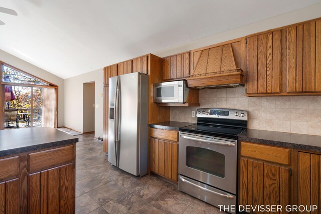 2766 48th Ave, Zeeland, MI 49464 - kitchen featuring stainless steel appliances, custom exhaust hood, dark countertops, brown cabinetry, and lofted ceiling