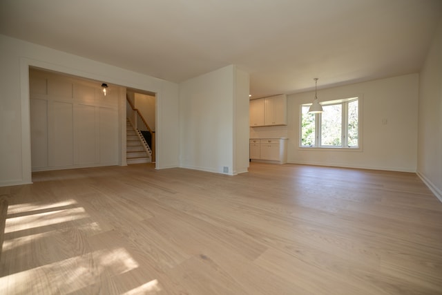 unfurnished living room featuring visible vents, light wood-type flooring, stairs, and baseboards