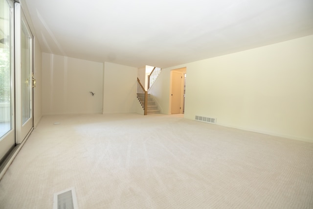 unfurnished room with visible vents, light colored carpet, and stairway