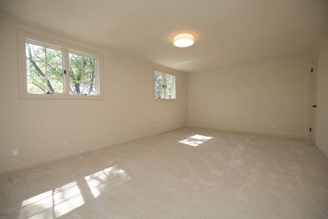 empty room featuring visible vents, light colored carpet, crown molding, and baseboards