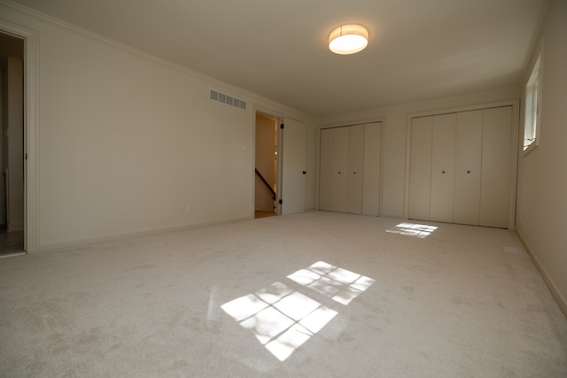 unfurnished bedroom featuring visible vents, two closets, carpet, crown molding, and baseboards