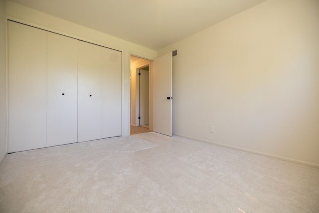 unfurnished bedroom with light carpet, visible vents, baseboards, and a closet