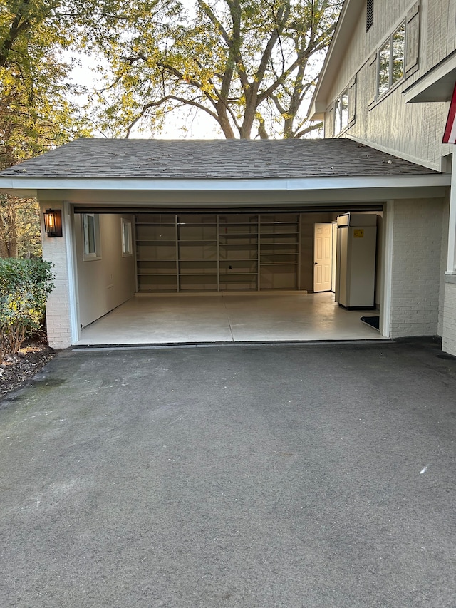 garage featuring an attached carport, driveway, and refrigerator