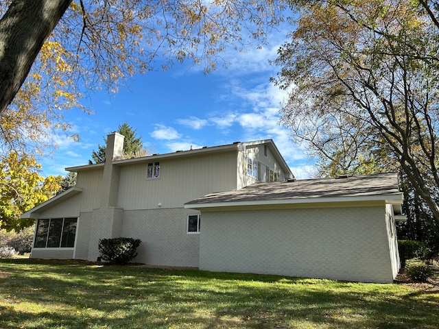 rear view of property with a lawn, brick siding, and a chimney