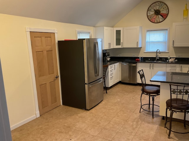 kitchen with a kitchen bar, appliances with stainless steel finishes, vaulted ceiling, sink, and white cabinets