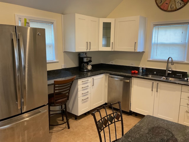 kitchen with appliances with stainless steel finishes, white cabinetry, dark stone counters, and sink