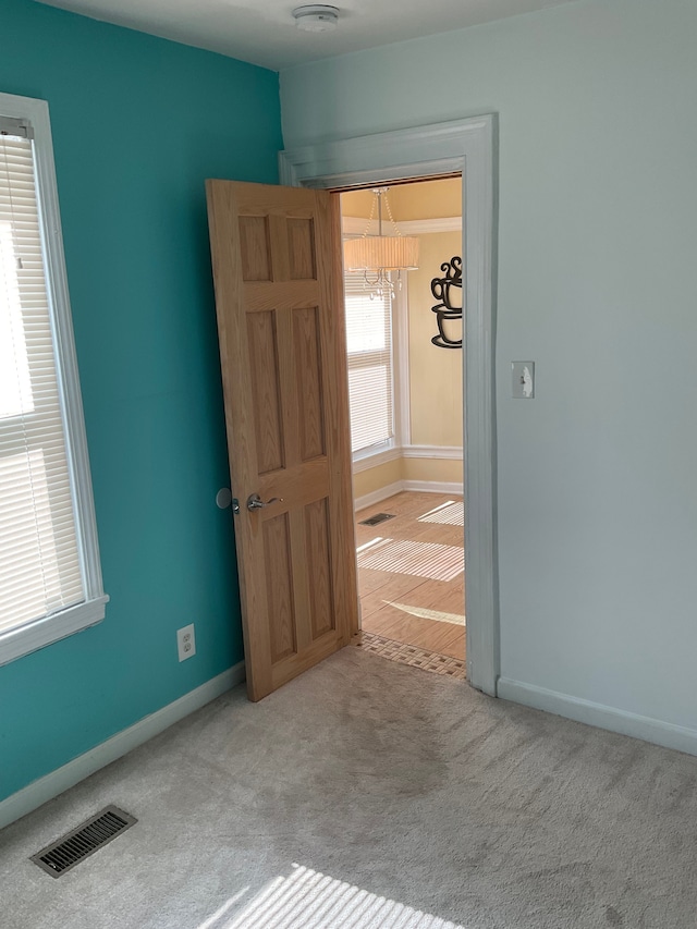 spare room featuring light carpet and an inviting chandelier