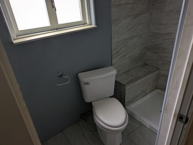 bathroom featuring toilet, tiled shower, and tile patterned flooring