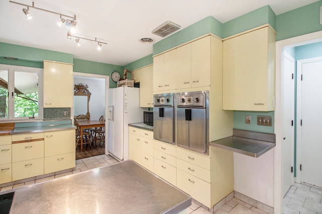 kitchen featuring cream cabinets, backsplash, white fridge with ice dispenser, and stainless steel counters