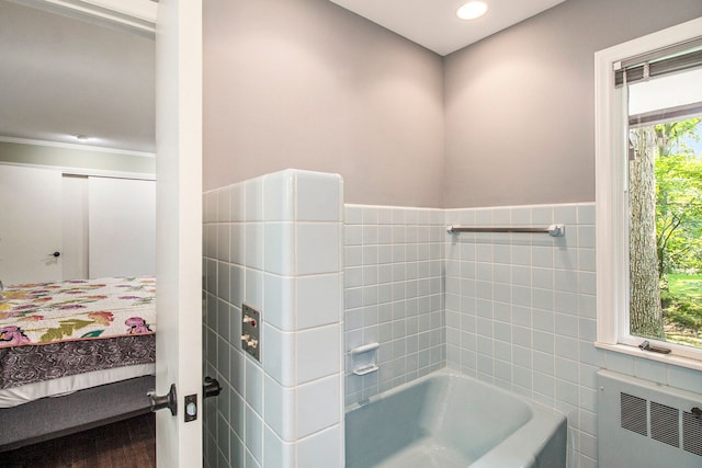 bathroom featuring plenty of natural light, a tub to relax in, radiator heating unit, and tile walls