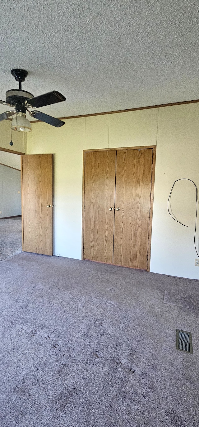 unfurnished bedroom with carpet flooring, ceiling fan, a textured ceiling, and a closet