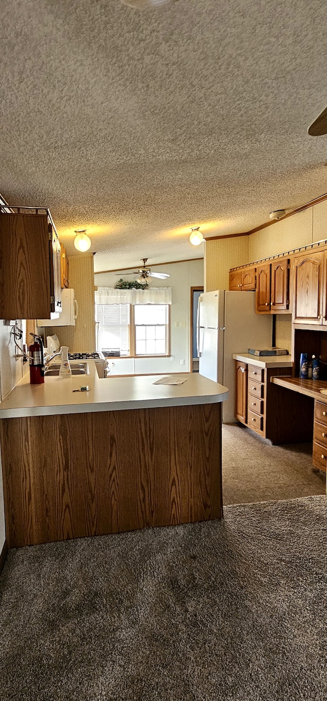 kitchen with kitchen peninsula, carpet, a textured ceiling, and white appliances