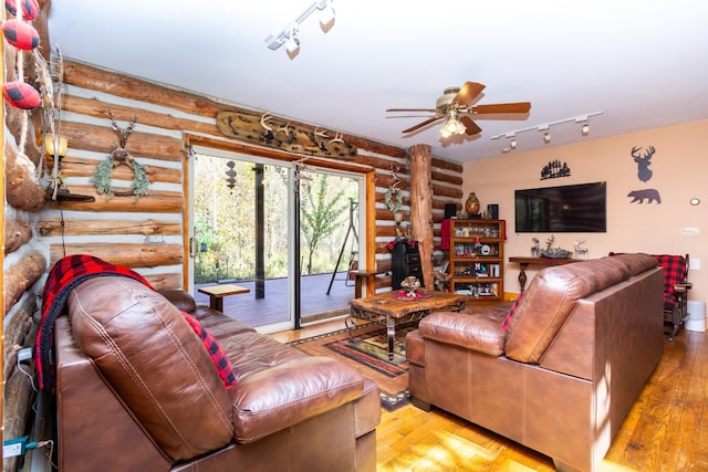 living room with rail lighting, ceiling fan, log walls, and light wood-type flooring