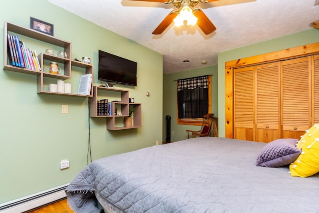 bedroom with a textured ceiling, ceiling fan, a baseboard heating unit, wood-type flooring, and a closet