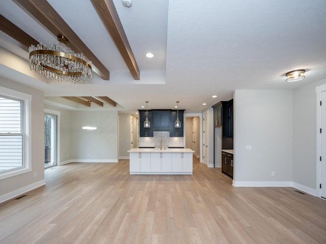 kitchen with backsplash, beam ceiling, decorative light fixtures, a center island with sink, and light hardwood / wood-style flooring