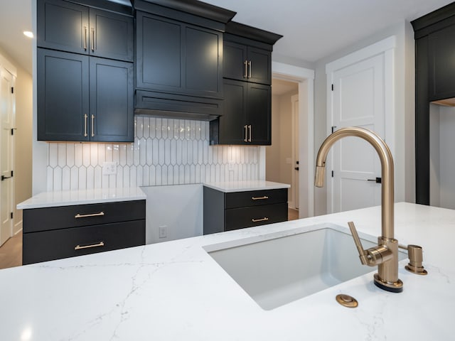 kitchen featuring decorative backsplash, light stone counters, and sink