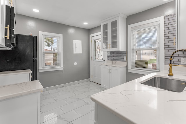 kitchen with light stone counters, white cabinetry, and sink