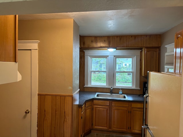 kitchen featuring white refrigerator, wooden walls, and sink