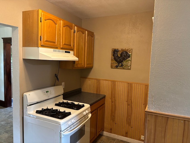 kitchen with a textured ceiling, wood walls, white gas range oven, and tile patterned floors