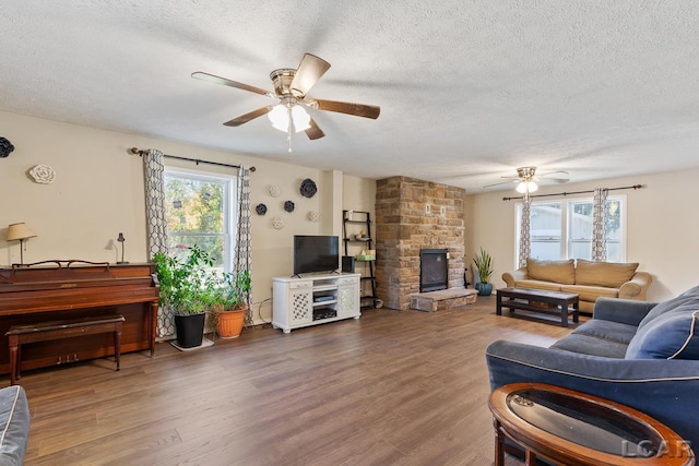 living room featuring a textured ceiling, a stone fireplace, ceiling fan, and dark hardwood / wood-style floors