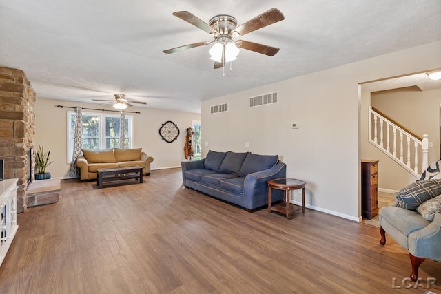 living room with a textured ceiling, hardwood / wood-style flooring, a stone fireplace, and ceiling fan