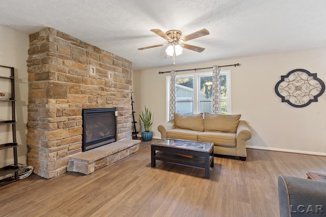 living room with hardwood / wood-style flooring, ceiling fan, a fireplace, and a textured ceiling