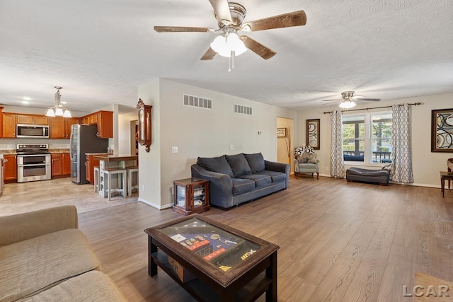 living room featuring ceiling fan with notable chandelier, a textured ceiling, and light wood-type flooring